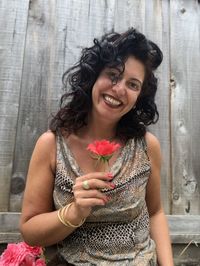 Portrait of smiling young woman holding flower standing against wooden wall