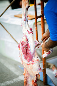 A man with a knife is cuttting the meat hanging on the hook.