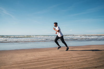 Full length of young man running on beach against sky