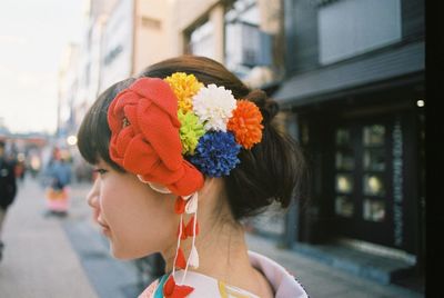 Side view of asian woman wearing flowers while standing building in city