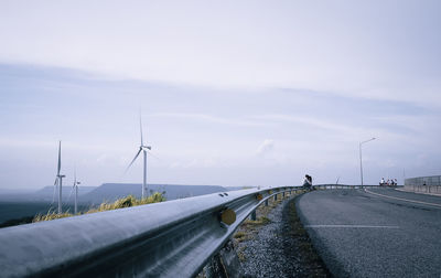 Road by wind turbines against sky