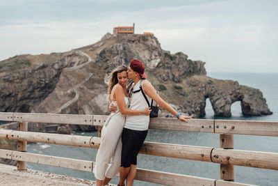 Couple embracing while standing by railing against sea