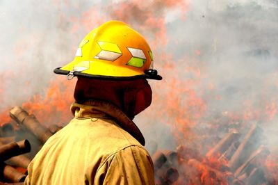 Side view of firefighter standing against fire