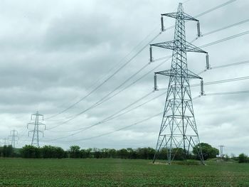 Low angle view of electricity pylon on field against sky