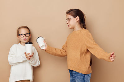 Portrait of young woman drinking wine while standing against wall