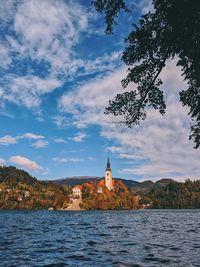 Buildings at waterfront on lake bled against cloudy sky in autumn.