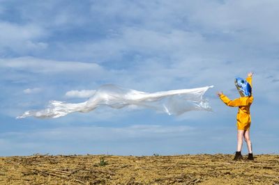 Woman wearing mask throwing fabric against sky