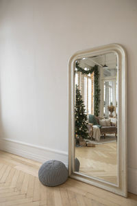 Spacious beautiful room with new year tree reflecting in mirror with beige frame and gray ottoman