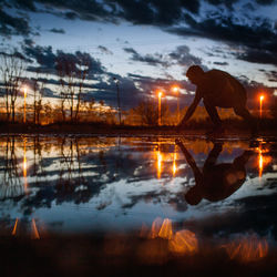 Man bending at lakeshore against sky during sunset