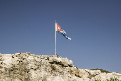 Low angle view of flag on rock against clear blue sky