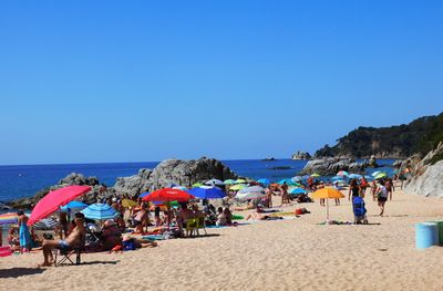 People at beach against clear blue sky