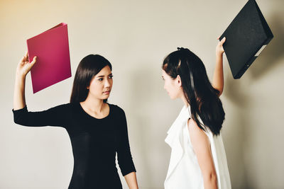 Businesswomen fighting with files while standing against wall