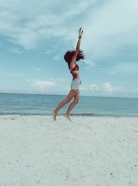 Side view of woman jumping at beach against blue sky