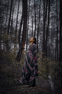 Woman standing by tree trunks in forest