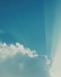 Low angle view of sunlight streaming through clouds