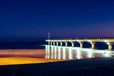 Bridge over sea against blue sky at night