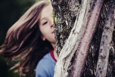 Close-up of girl hiding behind tree trunk