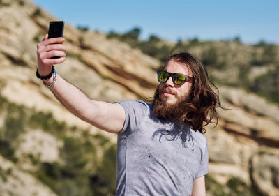 Young man wearing sunglasses talking selfie while standing on mountain