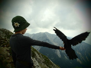 Side view of boy with bird on mountain against sky