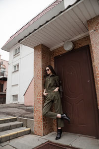 Full length front view portrait of tall slim brunette in green suit in urban setting, fashion  