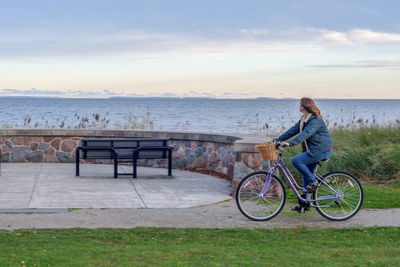 Woman on bicycle by sea against sky