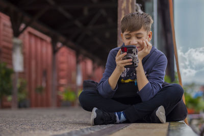 Full length of boy sitting in front of man holding mobile phone