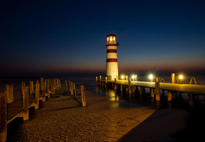 Pier leading towards illuminated lighthouse at beach