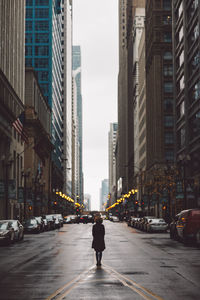 Rear view of woman standing on street amidst buildings in city