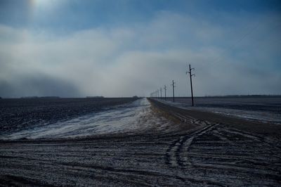 Country road with electricity pylons alongside against sky