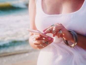 Midsection of woman using phone while standing at beach