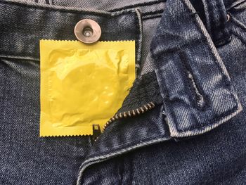 Close-up of yellow condom packet in jeans pocket