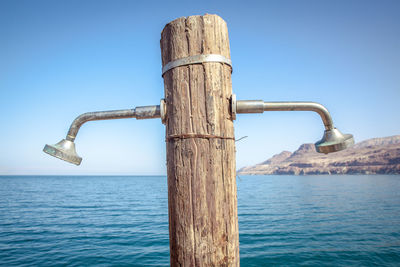 Wooden post in sea against clear blue sky