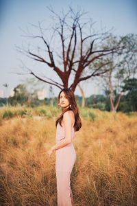 Portrait of young woman standing on grassy land against bare tree