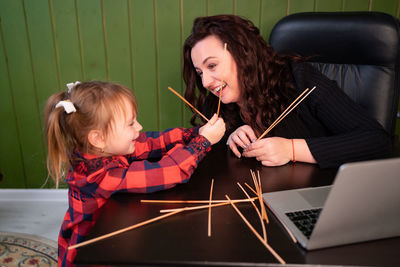 Smiling mother with daughter holding sticks at home