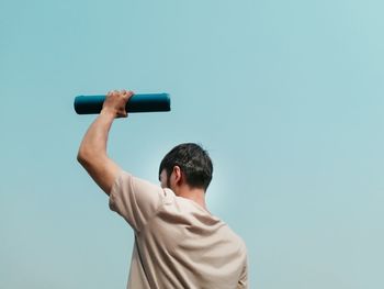 Rear view of man with arms raised against clear blue sky