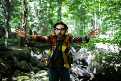 Young man with arms outstretched standing in forest