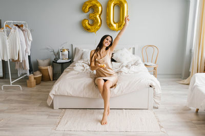 Cute woman with long hair is sitting on a bed in a cozy bedroom at home with a cake on a plate