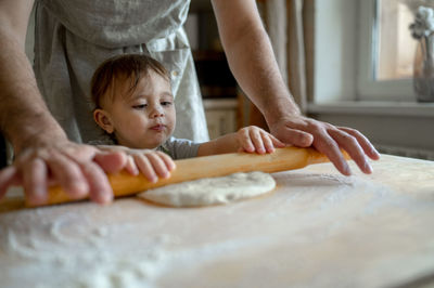 Man with baby boy rolling pizza dough in kitchen at home