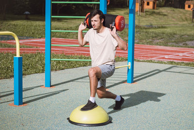 Man with a 10kg dumbbell with water on his shoulders does a lunge on a balance beam