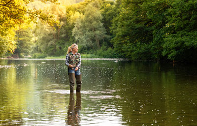 Young attractive woman is fishing with a spinning rod in the river on a clear summer sunny day.