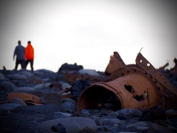 Close-up of shipwreck with people in background at beach against sky