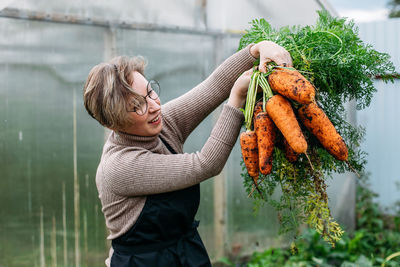 Smiling woman holding carrots at farm