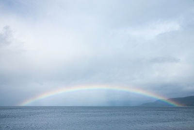 Rainbow over sea against cloudy sky