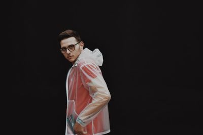 Portrait of young man standing against black background