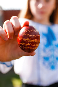 Ukrainian girl in vyshyvanka holding one colored red egg on nature background. easter, ukraine. 