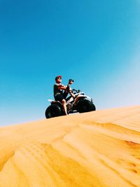 Young man riding bicycle on sand in desert