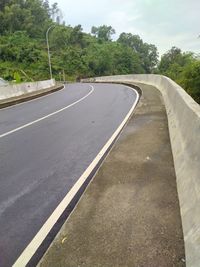 Empty road by trees in city against sky