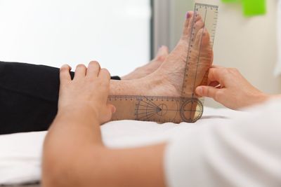 Cropped hands of doctor measuring man leg with ruler on bed at hospital