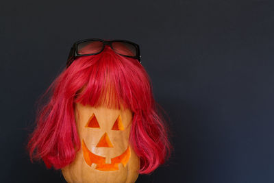 Close-up of jack o lantern with wig and sunglasses against black background