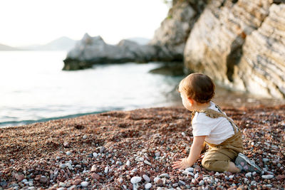 Rear view of boy sitting on rock at beach